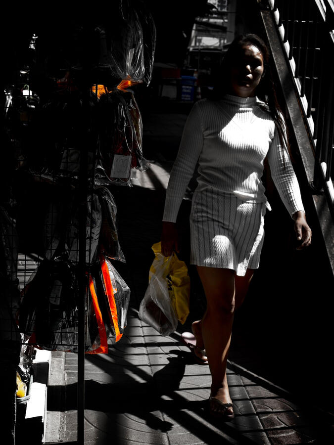 Woman walking through a shaft of sunlight on a Bangkok street.