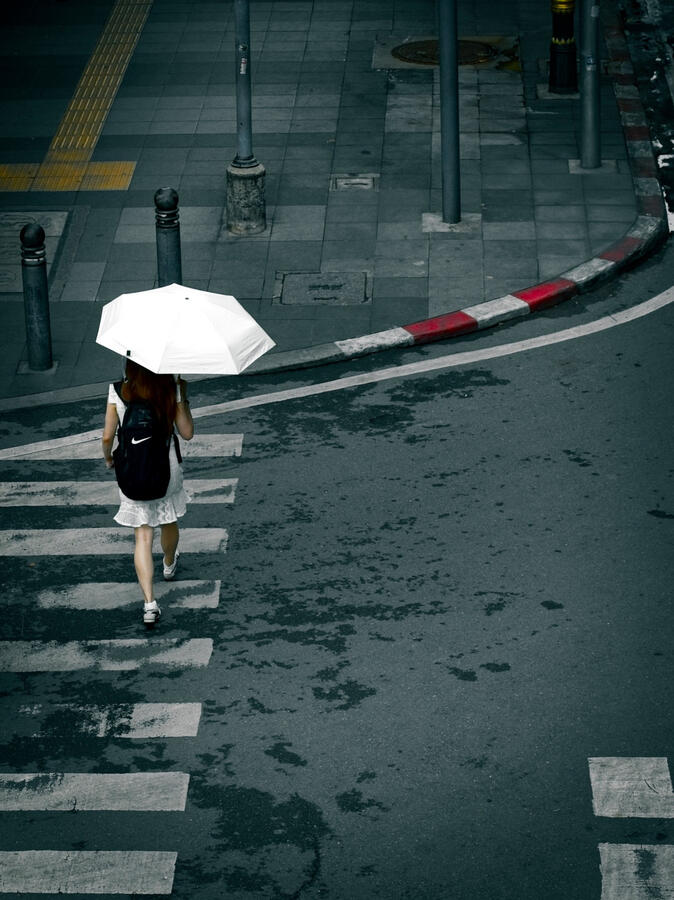 Woman carrying a white umbrella across a wet street in Bangkok, Thailand.