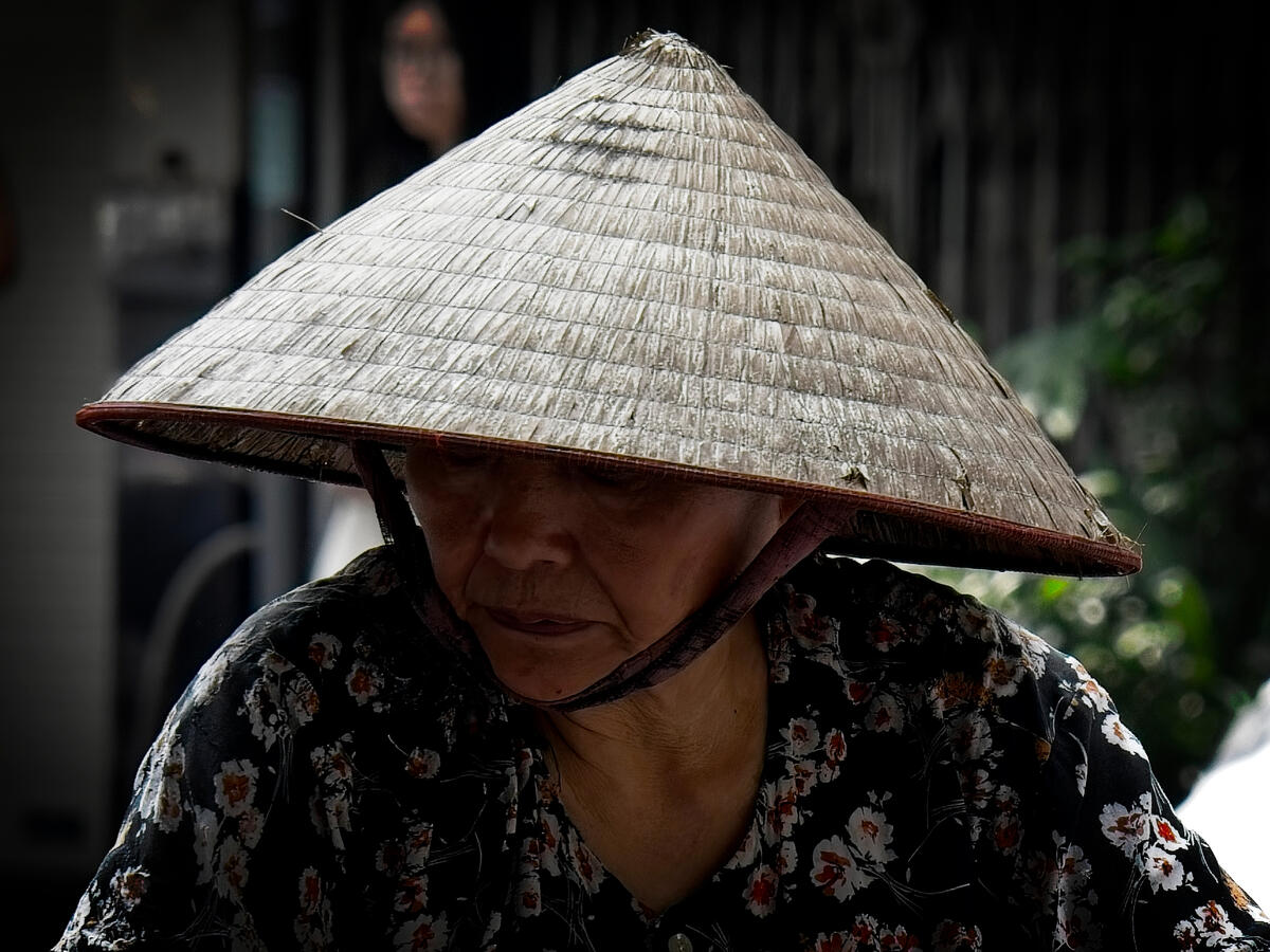 Close portrait of an older Vietnamese woman wearing a traditional conical hat in Hanoi, Vietnam.