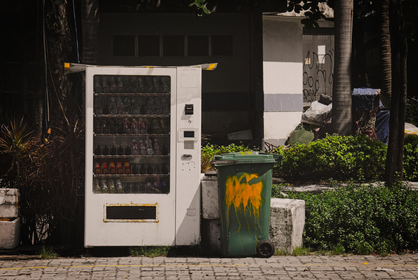A vending machine stands beside a weathered rubbish bin on a quiet street in Da Nang, Vietnam. An ordinary urban scene where convenience, neglect and everyday life exist side by side.