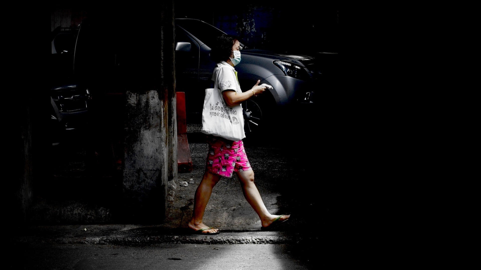 Bangkok, Thailand Woman walking through a beam of sunlight on a dark Bangkok street.